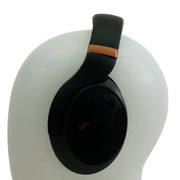 Black over-ear headphones with a metallic bronze accent on the headband, displayed on a white mannequin head against a white background.