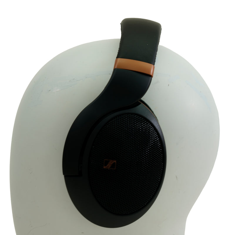 Black over-ear headphones with a metallic bronze accent on the headband, displayed on a white mannequin head against a white background.