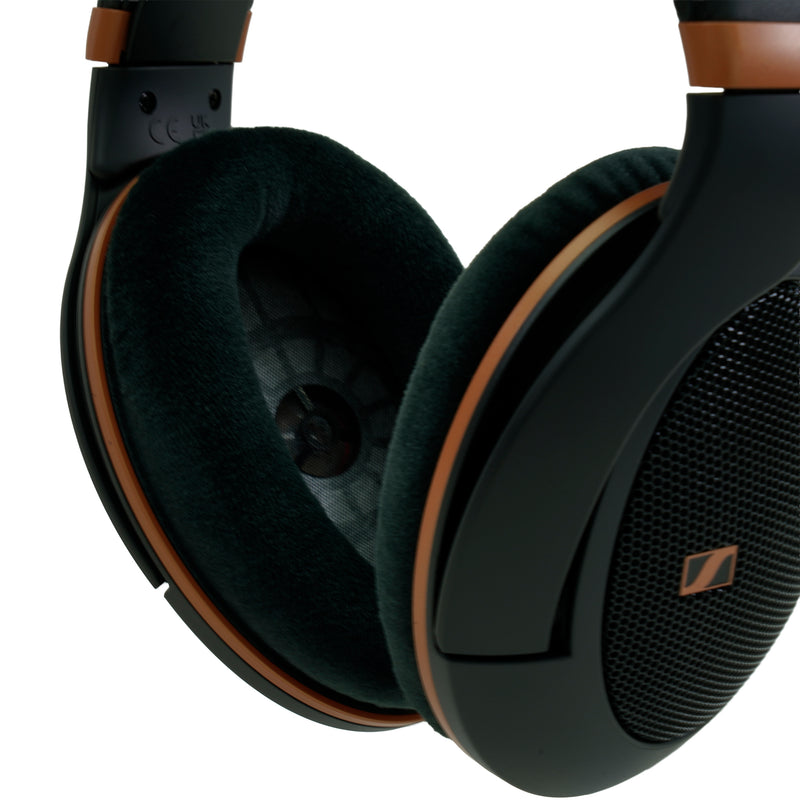 Close-up of black over-ear headphones with brown trim and dark green plush ear cushions, showing the outer earcup grille and part of the headband on a white background.