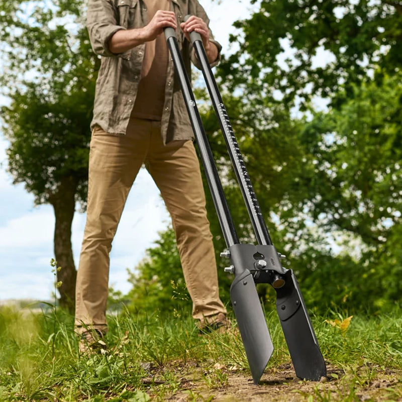 A man outdoors in a grassy field using a long-handled black post hole digger